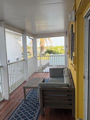 A covered outdoor area with a wooden deck, a blue patterned rug, and a sofa.