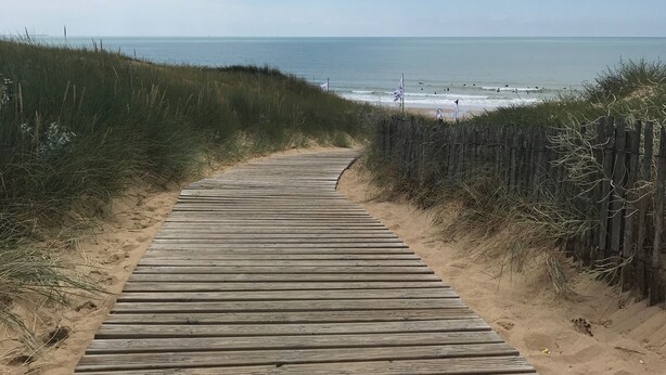 Ein hölzerner Steg führt zu einem Strand, der bewölkten Himmel darüber.