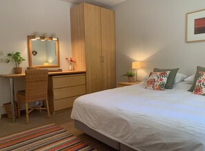 Une chambre à coucher comprenant un lit, un bureau, une chaise, une armoire, un miroir, une lampe et une plante en pot.