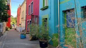 Eine enge Straße mit bunten Häusern, blauem Himmel und einigen Kübelpflanzen.