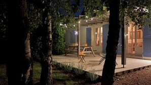 Eine Terrasse im Freien mit einem Holztisch und Stühlen, umgeben von Bäumen und erleuchtet mit Lichterketten.