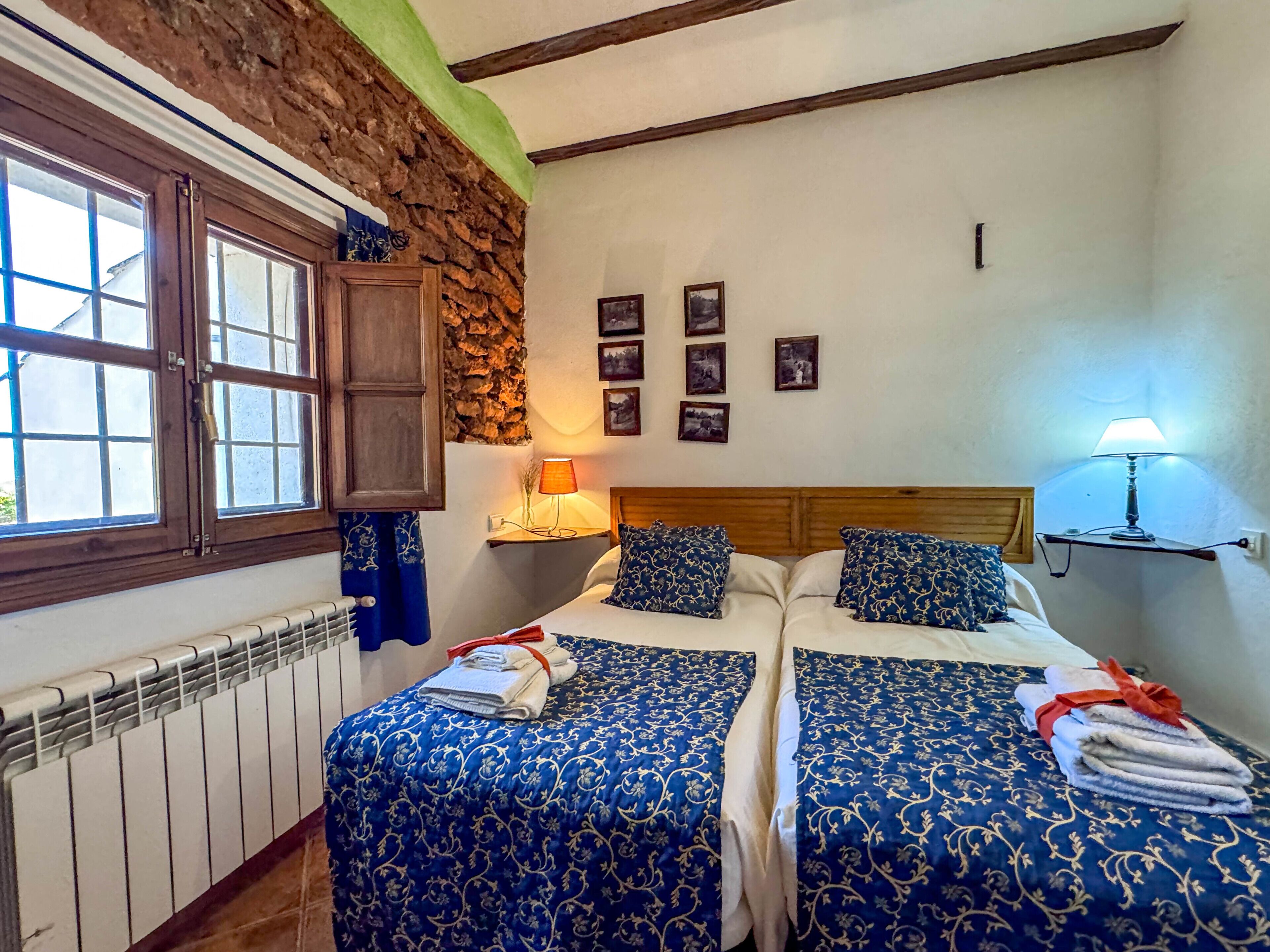 Un dormitorio con dos camas, una pared de piedra, techo de madera y una ventana.
