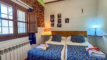Un dormitorio con dos camas, una pared de piedra, techo de madera y una ventana.