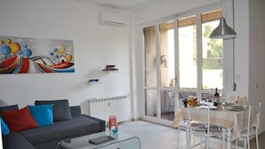 Una sala moderna con un sofá gris, una mesa de centro de vidrio y una zona de comedor con una mesa y sillas blancas.