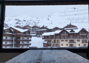 Een uitzicht op een bergresort met sneeuw, houten gebouwen en een skipiste op de achtergrond.