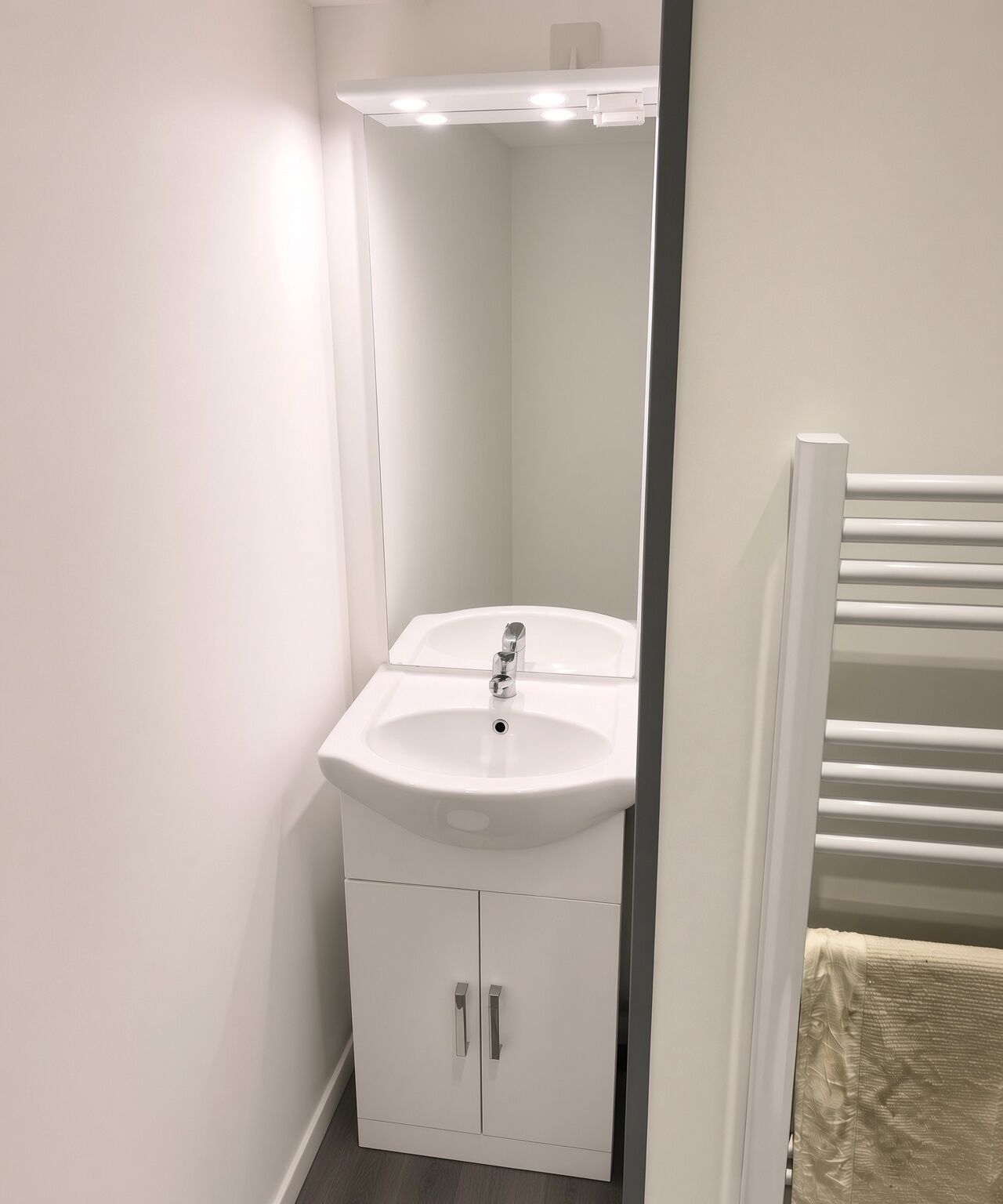 Un baño en esquina con un lavabo blanco, un espejo y un perchero.