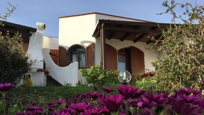 Una casa moderna con un diseño arquitectónico único, que presenta fachada blanca, contraventanas de madera y un accesorio de luz esférico en el jardín.