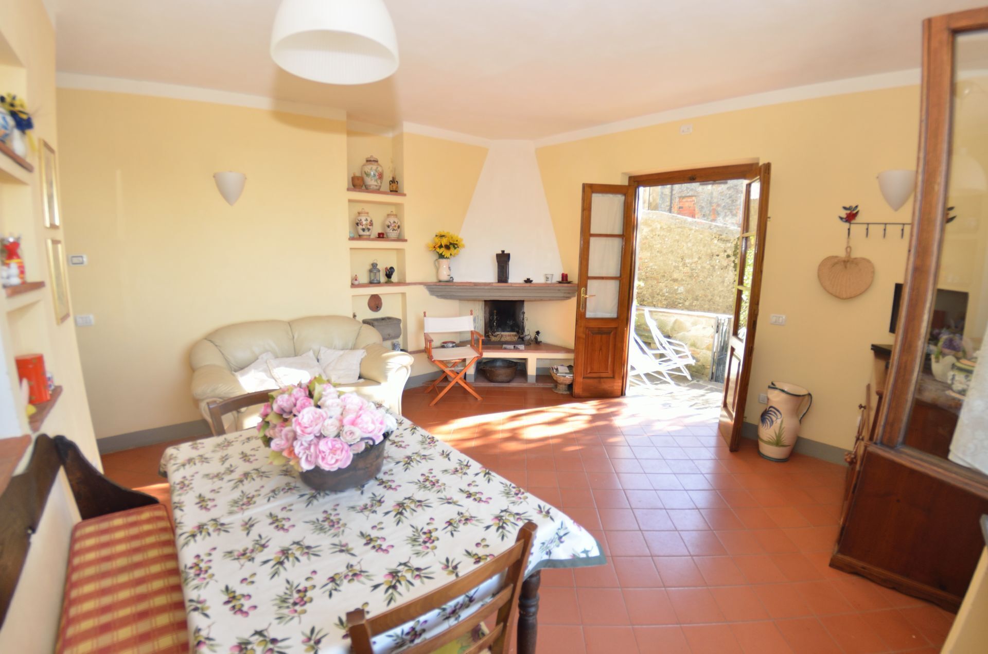 Een gezellige woonkamer met een bank, een eettafel met een bloemen tafelkleed, en een open haard.