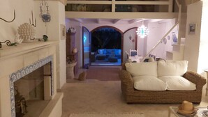 A cozy living room with a fireplace, a wicker sofa, and a staircase leading to an upper level. - SALENTO VILLA WITH POOL, GARDEN, TERRACES, NEAR THE SEA OF CASTRO (DISO)