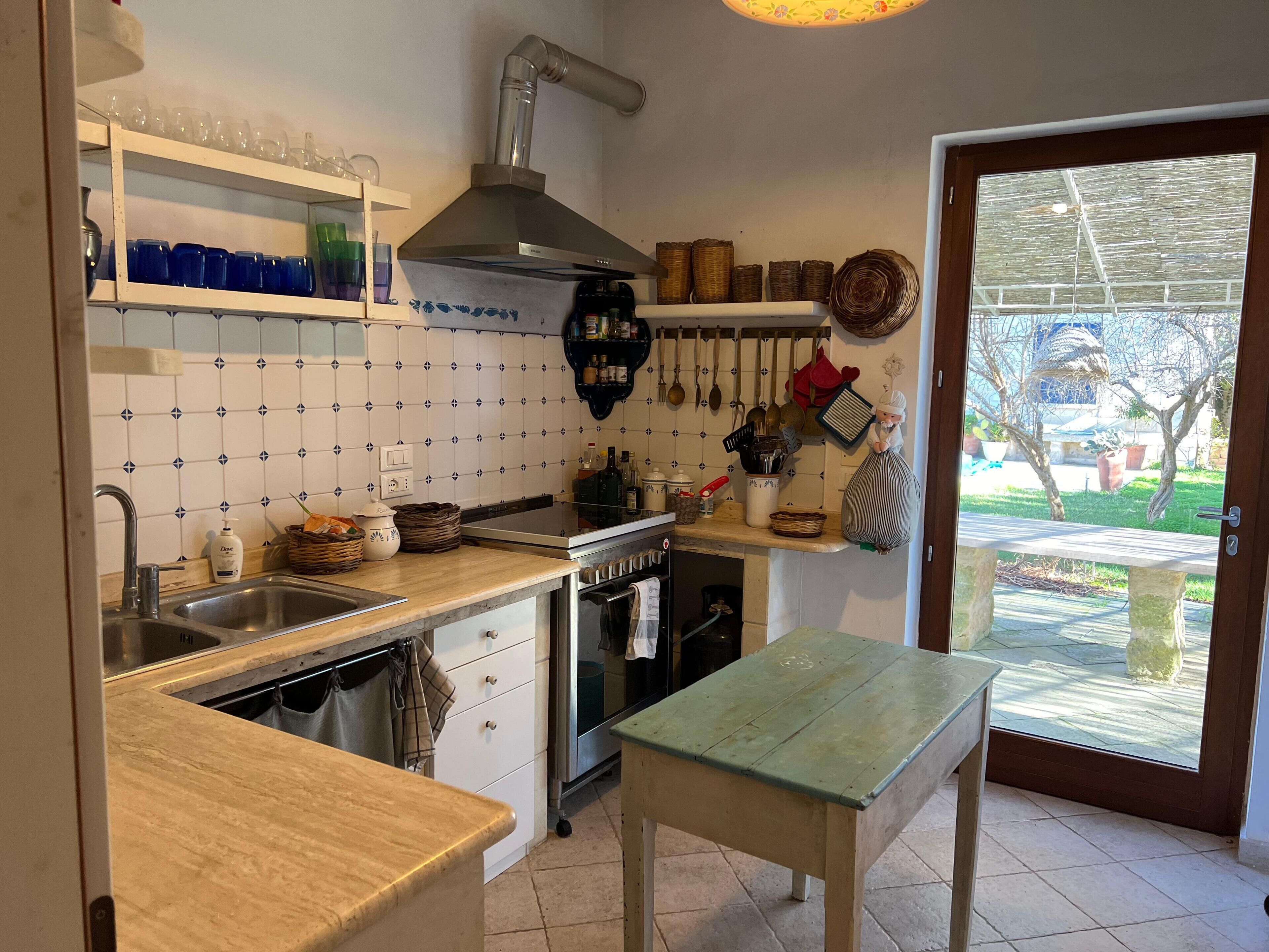 Una cocina con pileta, estufa y repisas con cristalería y cestas.