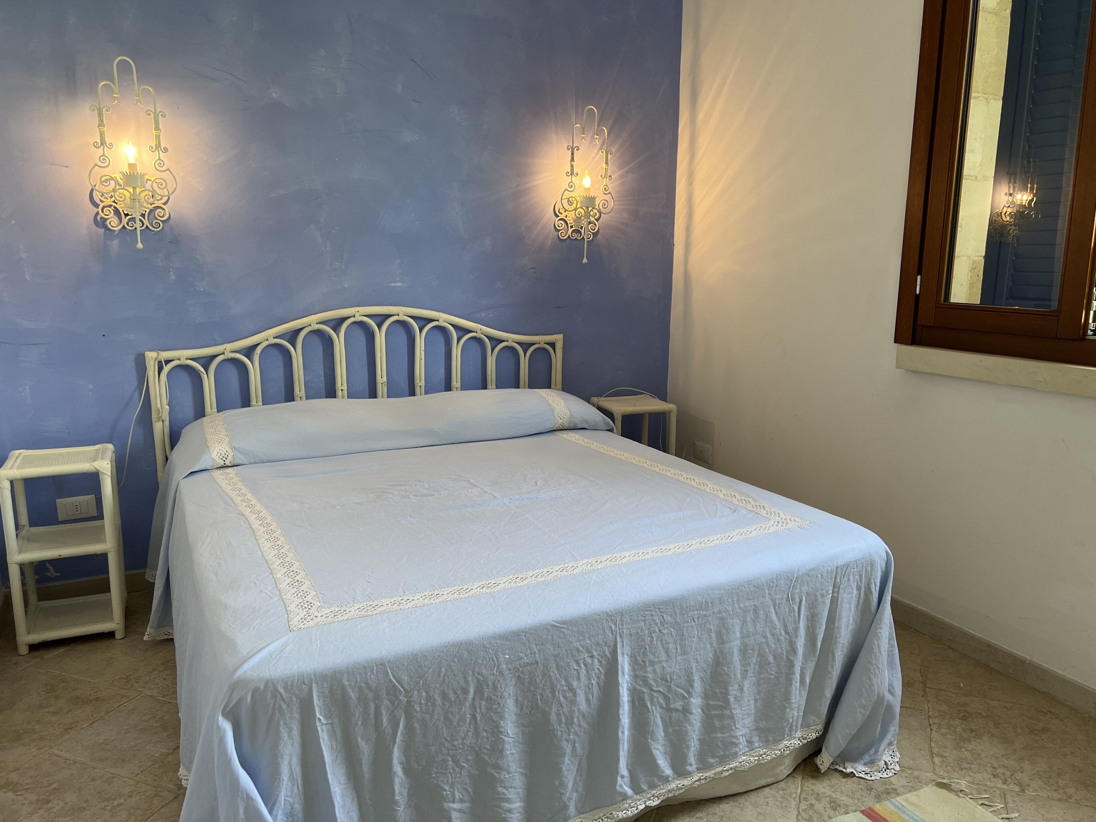 A bedroom with a bed, two bedside tables, and wall-mounted lights.