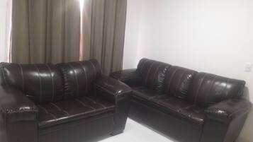 Un sofá de cuero marrón oscuro con chaise lounge, situado en una habitación de paredes blancas y una cortina.