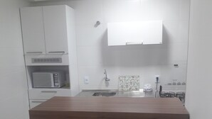 Una cocina con encimera de madera, armarios blancos, microondas y pileta.