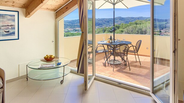 Een balkon met een tafel en stoelen, een glazen bijzettafeltje met een schaal, en uitzicht op het landschap.