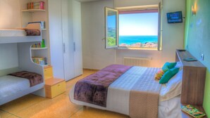 Een slaapkamer met een stapelbed, een bureau en een raam met uitzicht op zee.