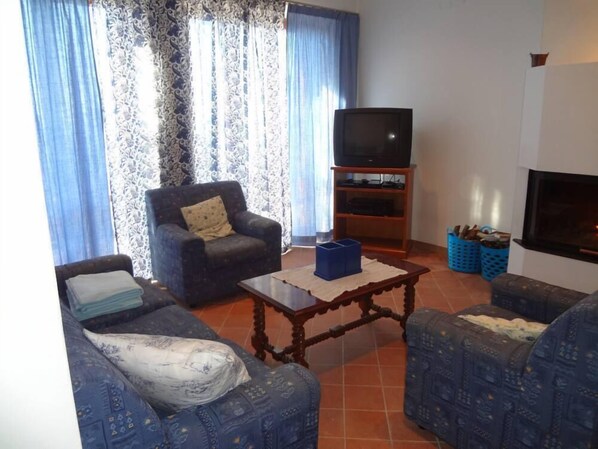 Una sala de estar con sofá, sillón, mesa de centro, televisor sobre un mueble bajo y chimenea.