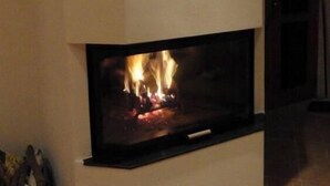 Una chimenea moderna con repisa blanca y frente de vidrio, mostrando fuego.