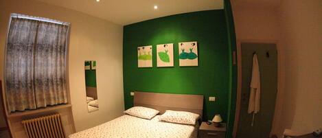 A bedroom with a bed, a nightstand, a mirror, a radiator, and a green wall with three animal-themed pictures.
