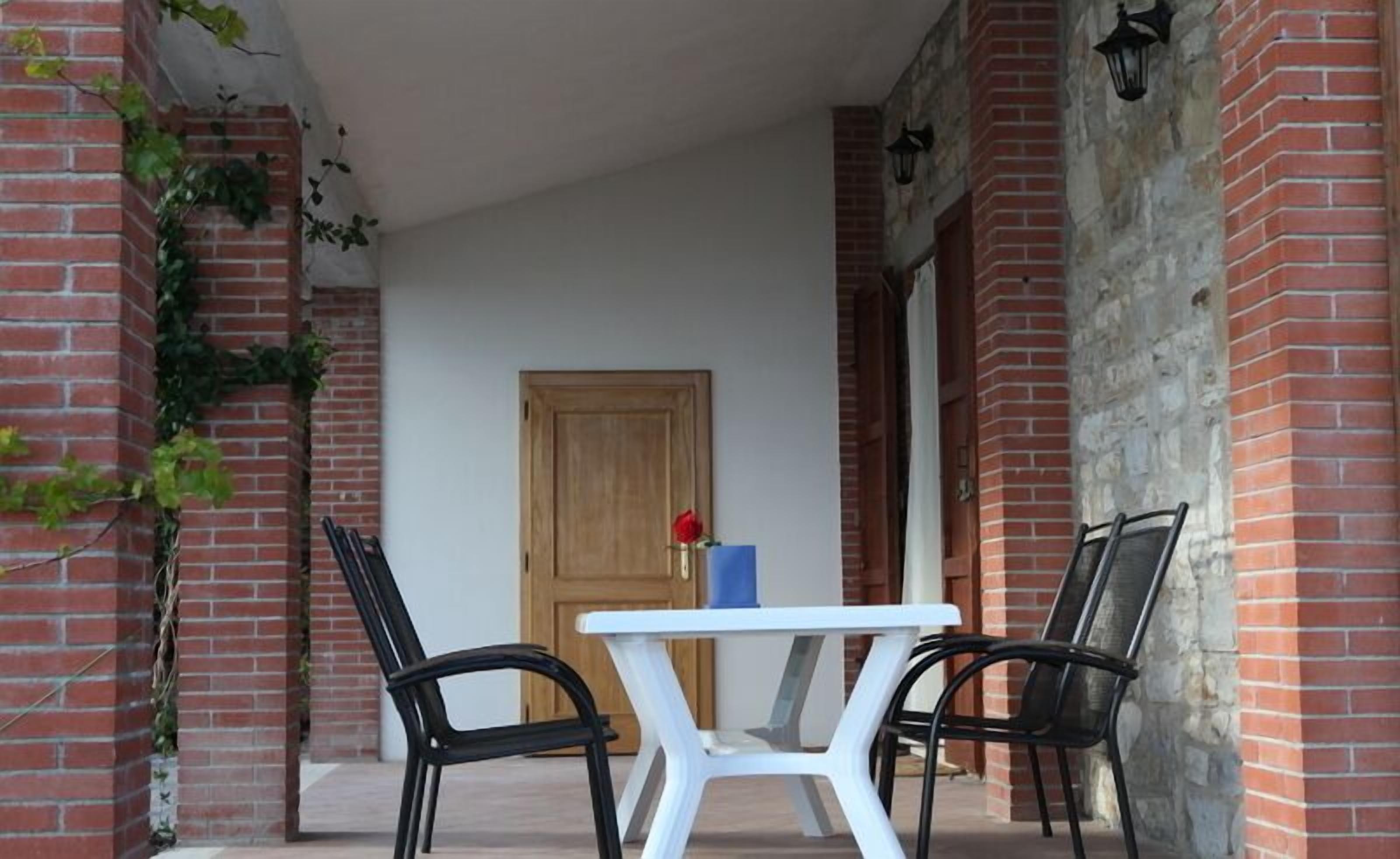 Eine Terrasse mit zwei schwarzen Stühlen, einem weißen Tisch, einer Holztür und Ziegelwänden.