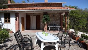 Una casa con techo de tejas, una chimenea de piedra y un porche cubierto con una mesa y sillas.