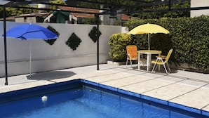 A swimming pool with two umbrellas, a table, and chairs. - Hotel Bella Vista (Villa Carlos Paz)