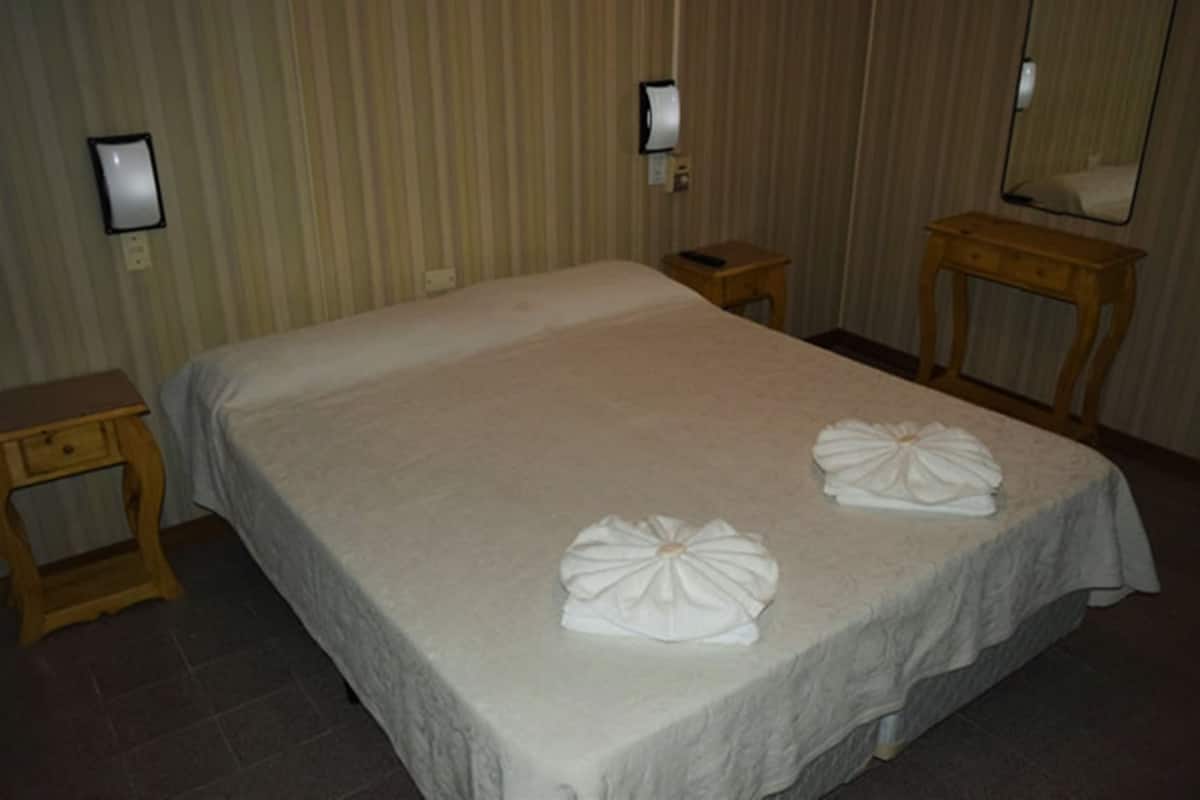Ein Hotelzimmer mit einem großen Bett, zwei Nachttischen, einem hölzernen Beistelltisch, einem Spiegel und einer Wandleuchte.