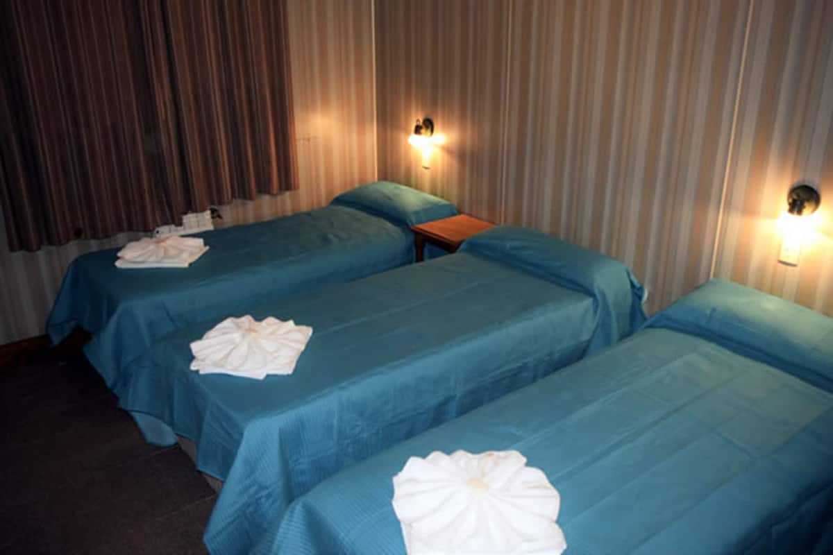 Ein Hotelzimmer mit zwei Einzelbetten, jeweils mit blauer Bettdecke und weißen Kissen. Zwei Wandlampen sorgen für Beleuchtung.