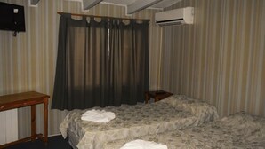 A hotel room with two beds, a wooden table, a TV, and an air conditioning unit. - Hotel Bella Vista (Villa Carlos Paz)