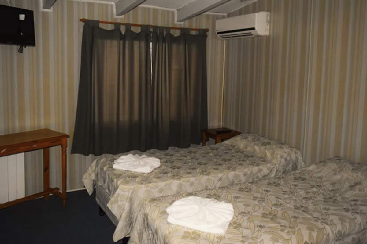 Ein Hotelzimmer mit zwei Betten, einem Holztisch, einem Fernseher und einer Klimaanlage.