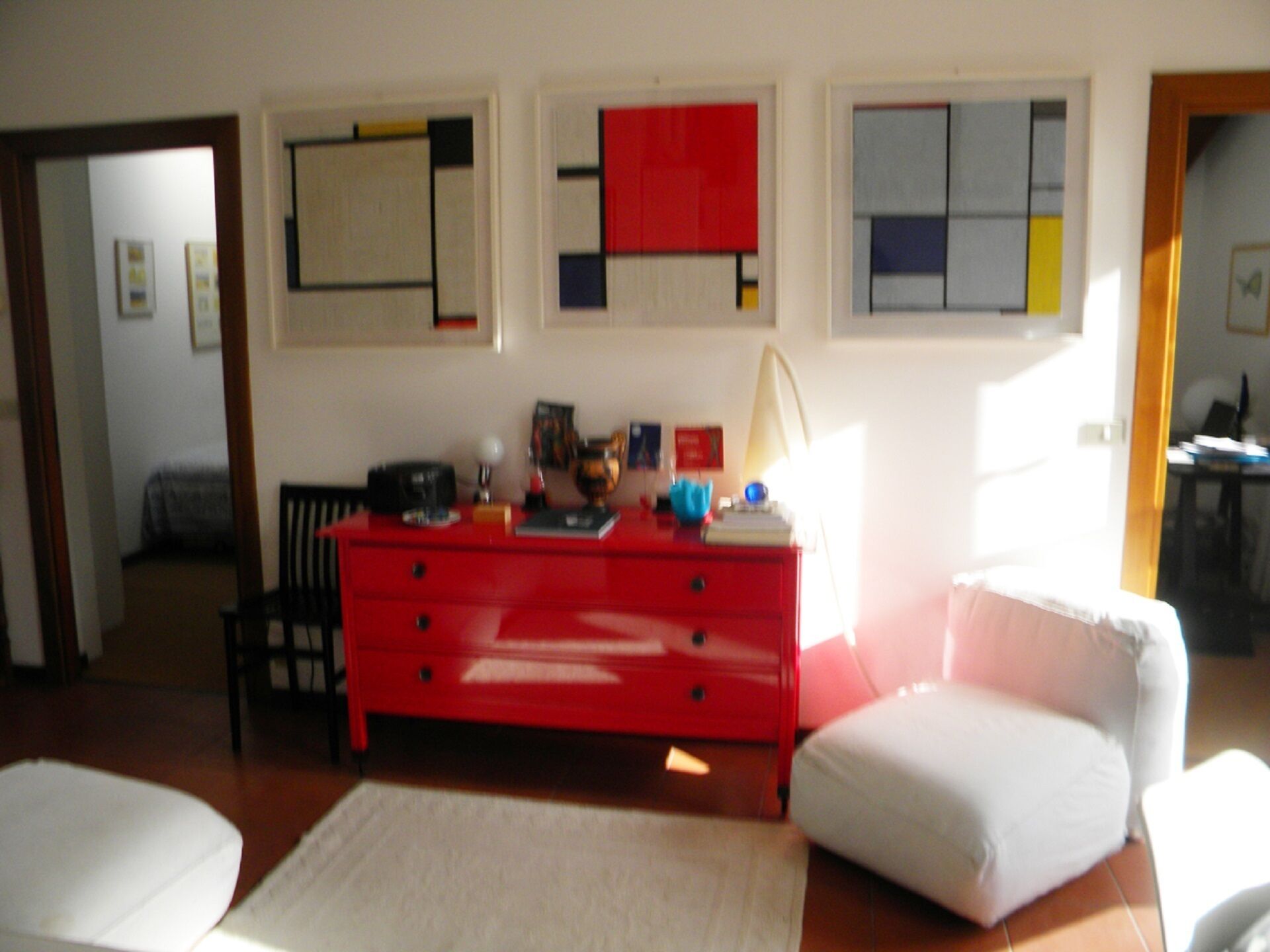 Un saló amb un taulell vermell, una butaca blanca i un sofà blanc. Hi ha quadres abstractes a la paret.