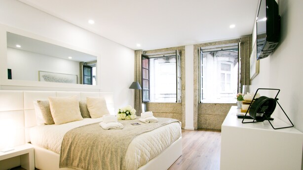 Un dormitorio moderno con una cama grande, una mesita de noche, un televisor de pantalla plana en la pared y una ventana con cortinas.