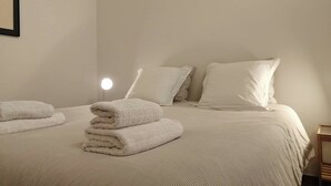 Un lit bien fait, recouvert d’une couverture blanche, avec une lampe de chevet ronde et deux oreillers.