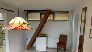 Ein kompakter Wohnbereich mit Holztisch, Korbsessel, kleinem weißen Heizkörper und einer Treppe.