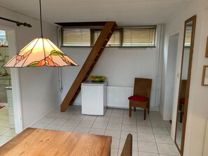 A compact living space with a wooden table, a wicker chair, a small white radiator, and a staircase.