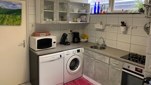 Eine kleine Küche mit Waschmaschine, Mikrowelle, Spüle und einem kleinen Fenster mit Pflanzen.
