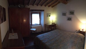 Une chambre à coucher comprenant un lit, un bureau, une chaise, une armoire et une fenêtre avec des rideaux.