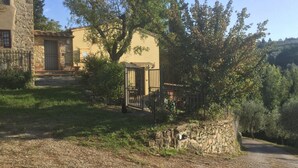 Un bâtiment rustique en pierre, doté d’une façade jaune, d’une entrée fermée par un portail et d’un mur en pierre.