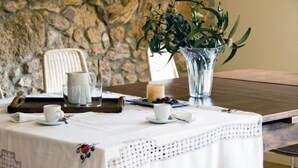 Una mesa de comedor con mantel blanco, un florero con follaje verde, una vela y una jarra.