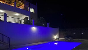 A swimming pool with blue lighting, a multi-story building with balconies, and outdoor seating. - Luxury Private 3 bedroom (sleeps 6)Villa, Breathtaking Views & 200mbps Wi-Fi (Paphos)