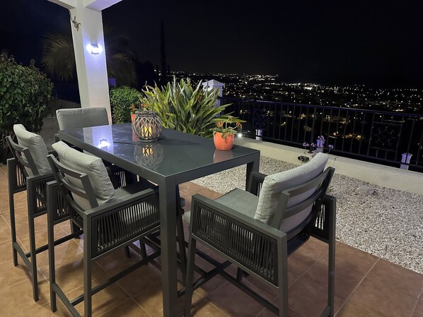 A patio with a table and chairs, a potted plant, and a view of a cityscape at night. - Luxury Private 3 bedroom (sleeps 6)Villa, Breathtaking Views & 200mbps Wi-Fi (Paphos)