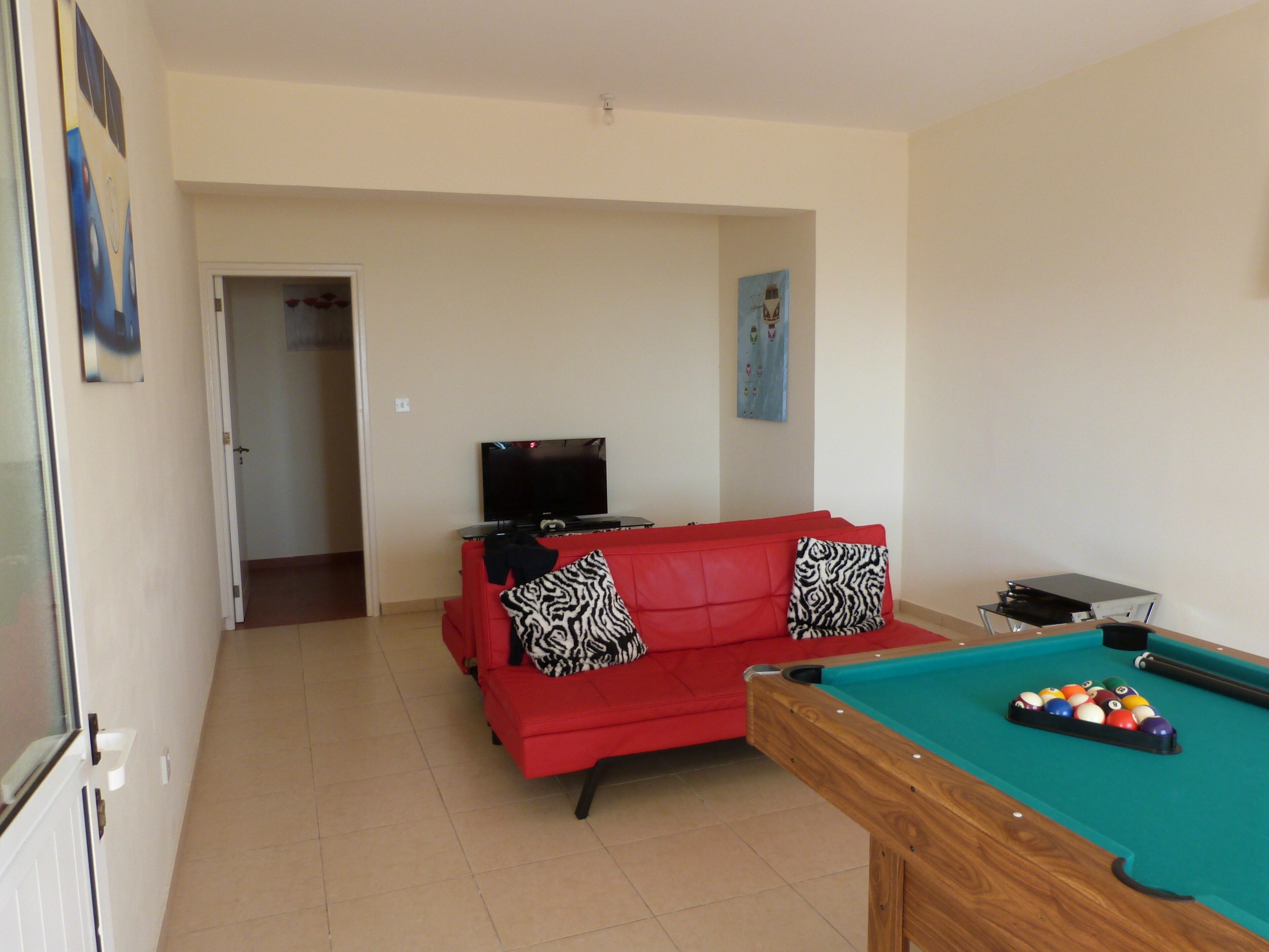 A living room with a red sofa, a pool table, and a television.