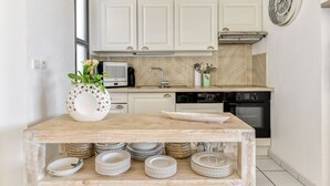 A kitchen with white cabinets, a microwave, a sink, and a stove. There is a wooden table with plates and a vase with flowers. - Between land and sea in the Cathar region (Durban-Corbières)