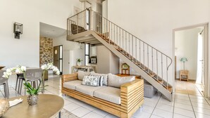A modern living room with a wooden sofa, a dining area with chairs, a staircase, and a kitchen in the background. - Between land and sea in the Cathar region (Durban-Corbières)