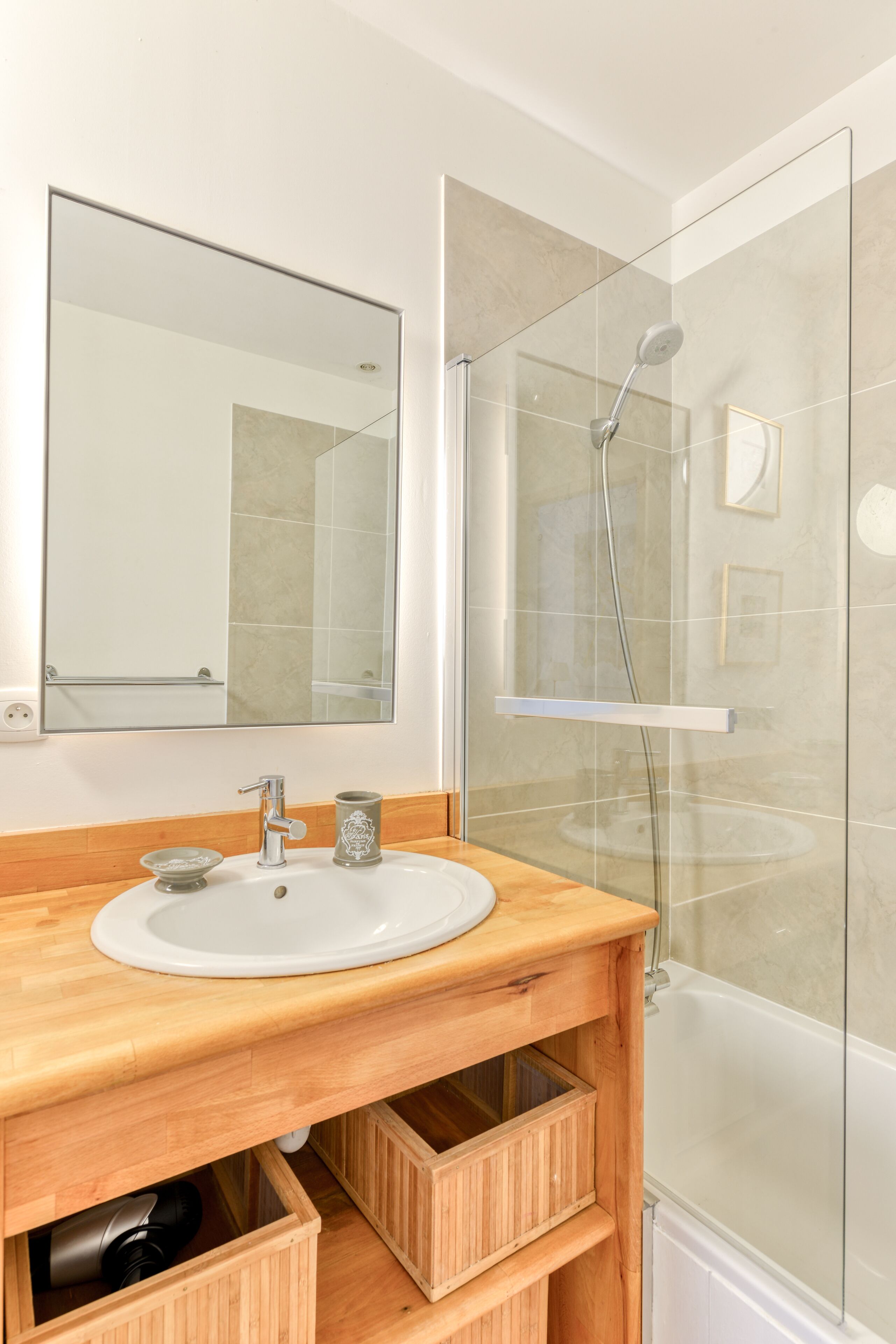 A modern bathroom with a wooden vanity, a large mirror, and a glass-enclosed shower.