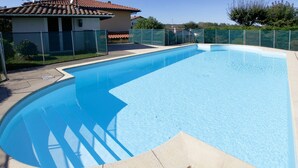 A rectangular swimming pool with a clear blue water surface, surrounded by a beige tiled deck and a green fence. - house / villa - Hendaya with swimming pool (Hendaye)