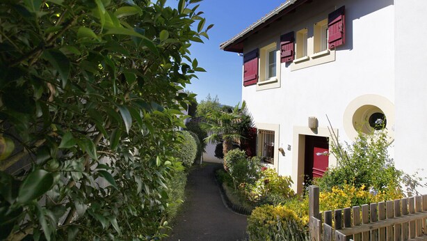 A narrow pathway leading to a white building with red shutters and a small porch. - house / villa - Hendaya with swimming pool (Hendaye)