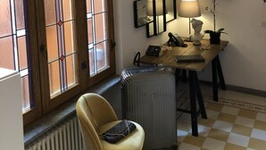 Una habitación con un gran ventanal de arco, un radiador, un escritorio con lámpara y una silla.