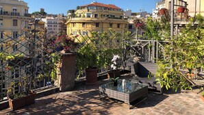 Una terraza en la azotea con plantas en macetas, una mesa con cubierta de vidrio y un sofá de mimbre.