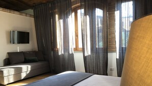 Un dormitorio con cama, sofá, televisión montada en la pared y ventana con cortinas.