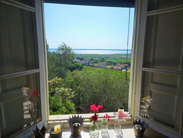 A window with a view of a coastal landscape, a table with candles, and decorative vases.